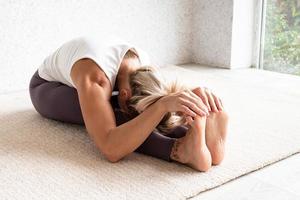 Blonde woman practising yoga at home, stretching photo