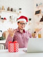 Man in santa hat greeting his friends in video chat or call on laptop photo