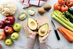 Female hands holding avocado for detox diet top view flat lay