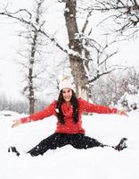 Joven mujer morena en suéter rojo jugando con la nieve en el parque foto