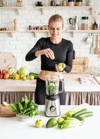 Young blond smiling woman making celery smoothie at home kitchen