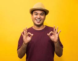 Young asian man showing hand ok sign on yellow background.
