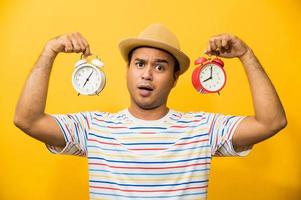 Young asian man holding the alarm clock on yellow isolated background. photo