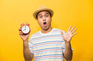 Young asian man holding the alarm clock on yellow isolated background. photo