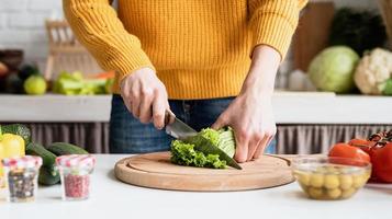 Woman preparing greek salad in kitchen cutting lettuce photo