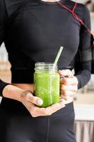 Woman in black sportswear holding a jar of green smoothie photo