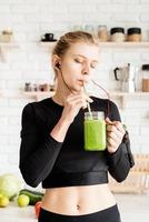 Mujer joven bebiendo batido verde saludable en la cocina foto