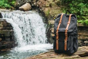 Mochila turística excursionista hipster en el fondo del río y la cascada foto