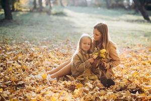 madre e hija sentadas y divirtiéndose en el parque de otoño.