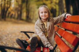 una niña con un vestido amarillo y un abrigo beige camina en el parque de otoño foto