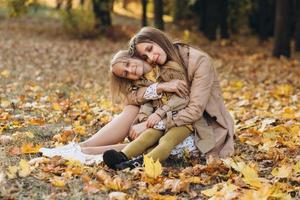 Mother and her daughter sitting among leaves in the autumn park. photo