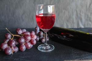 Botella de vino tinto y vino con uvas sobre fondo negro foto