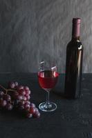 Botella de vino tinto y vino con uvas sobre fondo negro foto
