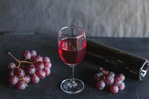 Botella de vino tinto y vino con uvas sobre fondo negro foto