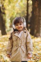 Happy little girl listening to music on headphones in the autumn park. photo