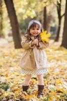 Happy little girl holding a yellow maple leaf in the autumn park photo