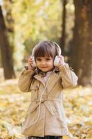 niña feliz escuchando música con auriculares en el parque de otoño. foto