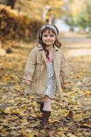 Happy little girl in a beige coat walks in the autumn park photo