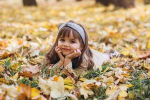 niña se encuentra entre las hojas amarillas en el parque de otoño foto