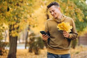 chico feliz sonriendo y hablando por teléfono en el parque de otoño foto