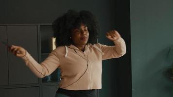 Woman with earphones and smartphone dances in living room video