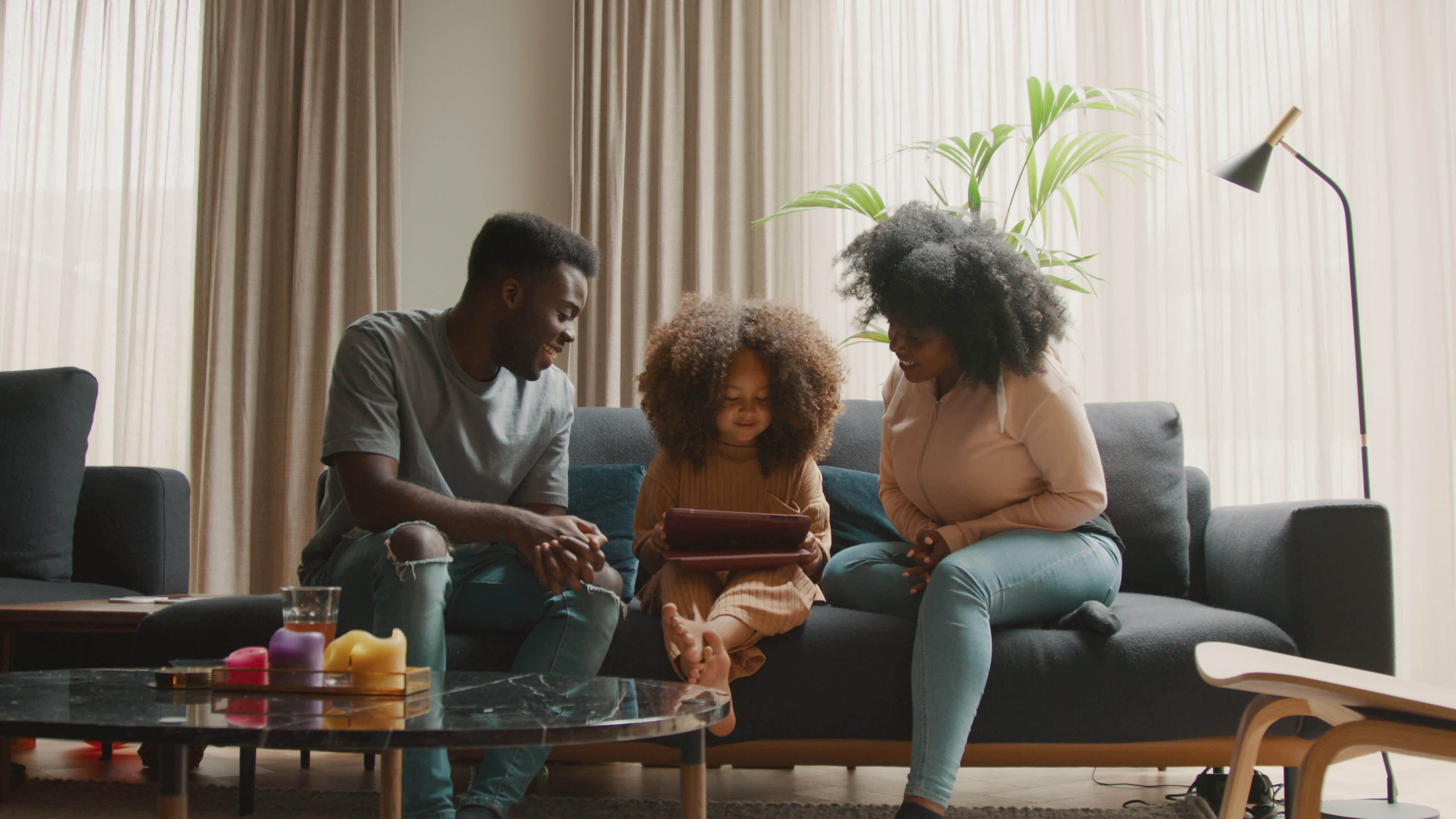 Man and woman on sofa watching girl with tablet