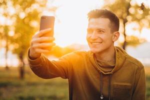 chico sosteniendo un ramo de hojas y tomando selfie en el parque foto