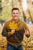 chico sonriendo y sosteniendo un ramo de hojas de otoño en el parque foto