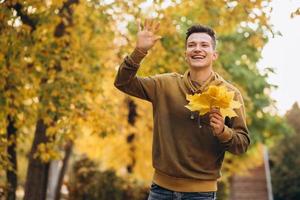 Retrato de chico guapo y feliz sonriendo y saludando en el parque de otoño foto