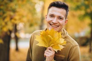 Guy smiling and holding a bouquet of autumn leaves in the park photo