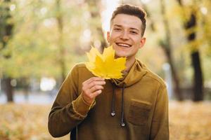 chico sonriendo y sosteniendo un ramo de hojas de otoño en el parque foto