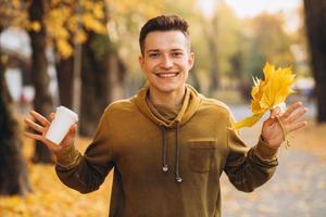 chico con un ramo de hojas sonriendo y bebiendo café en otoño foto