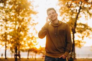 chico feliz sonriendo y hablando por teléfono en el parque de otoño foto