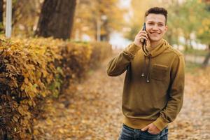 chico feliz sonriendo y hablando por teléfono en el parque de otoño foto
