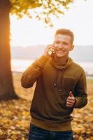 chico feliz sonriendo y hablando por teléfono en el parque de otoño foto