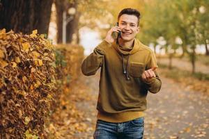 chico feliz sonriendo y hablando por teléfono en el parque de otoño foto