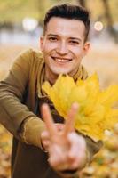 chico sonriendo y sosteniendo un ramo de hojas de otoño en el parque foto