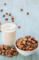 Almendras en recipiente blanco con vaso de leche fondo azul foto