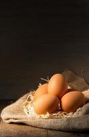 Huevos orgánicos frescos en arpillera con pasto seco sobre mesa de madera foto