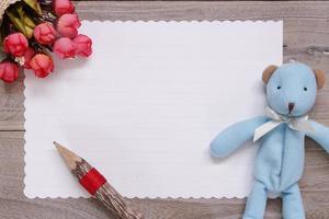 Wooden table white letter paper blue bear doll pencil rose flower photo