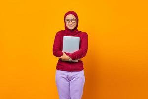 Portrait of smiling Asian woman bring laptop over yellow background photo