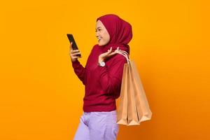 Hermosa mujer asiática sosteniendo bolsas de la compra y usando un teléfono inteligente foto