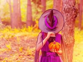 niña en disfraz de halloween con sombrero sobre los ojos con calabaza naranja foto