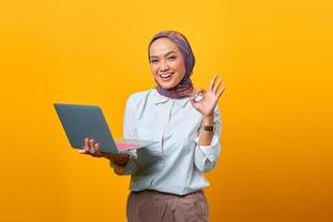 Beautiful Asian woman holding laptop smiling and showing okay sign