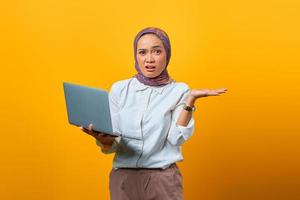 Portrait of surprised Asian woman holding laptop with confused face photo