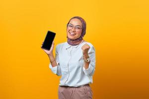 Mujer asiática mostrando la pantalla en blanco del teléfono inteligente y celebrando la suerte foto