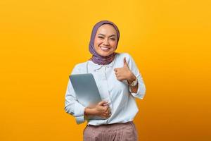 Asian woman holding laptop smiling and showing thumbs up sign photo