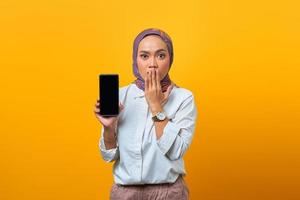 Conmocionada mujer asiática mostrando la pantalla del teléfono inteligente en blanco
