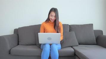 Young asian woman uses a laptop on the couch video