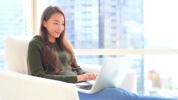 Young asian woman uses a laptop on the couch video